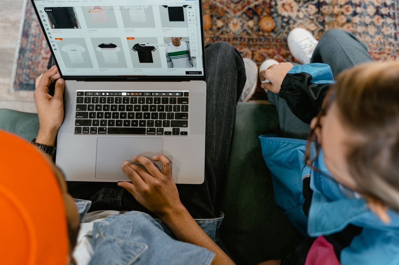 Two people browsing an online clothing store on a laptop from above.